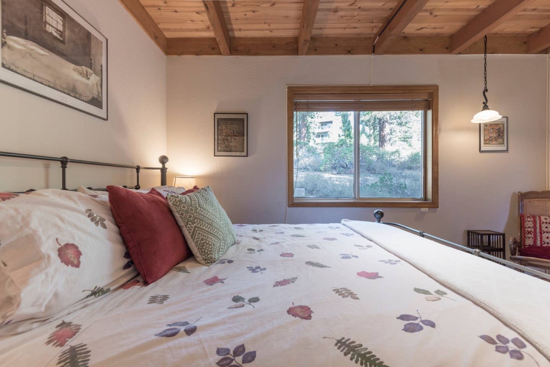 Queen bedroom with floral quilt and forest-view window